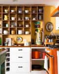 Colorful kitchen with open shelving displaying dishes, orange appliances, and a wooden island with grapes.