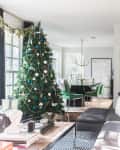 Living room with a decorated Christmas tree, gray sectional sofa, and dining area with green chairs in the background.