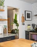Modern kitchen with subway tile backsplash, open shelves, potted plants, stainless steel stove, and wooden cutting board.