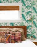 Bedroom with tropical leaf wallpaper, brown leather headboard, fur throw, and colorful patterned pillows.
