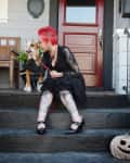 Person with red hair and tattoos sitting on porch steps with a dog, next to a carved pumpkin.