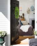 Open black door with green wreath leading to cozy living room, featuring a fireplace, white decor, and plush seating.