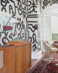 Dining room with patterned walls, round table, cushioned chairs, and a plant centerpiece on a red patterned rug.