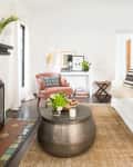 Living room with white sofa, patterned cushions, round metal coffee table, fireplace, and pink armchair.