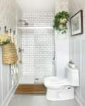 Bathroom with white subway tile shower, hexagonal floor tiles, hanging plant, woven basket, and framed wall art.