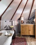 Attic bathroom with freestanding tub, brick accent wall, wooden vanity, and sloped ceiling beams.