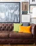 Brown leather sofa with green and yellow pillows, framed art, and a vintage license plate on the wall.