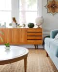 Mid-century modern living room with a teal sofa, wooden sideboard, globe, and geometric wall art.