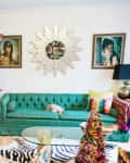 Colorful living room with a decorated Christmas tree, green sofa, vibrant artwork, and a sunburst mirror.