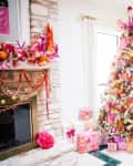 Festive living room with a decorated Christmas tree, colorful ornaments, gifts, and a vibrant mantel display.
