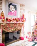 Festive living room with a decorated Christmas tree, colorful garlands on the fireplace, and wrapped gifts.