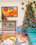 Festive living room with a decorated Christmas tree, colorful art, a "Merry + Bright" banner, and a cat on a teal sofa.