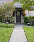 Pathway leading to a house entrance with black and white curtains, skeleton flamingo decorations, and green shrubs.