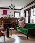 Living room with green sofa, pink chairs, books on mantel, and abstract art above fireplace.