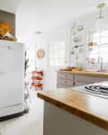 Retro-style white fridge in a bright kitchen with wooden countertops, red cart, and wall decor.