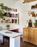 Home office with wooden desk, bookshelves, potted plants, and a gray sofa with cushions.