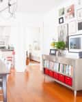Dining room with dark wood table, silver chairs, large nest painting, and wall art gallery. Metal bookshelf with red bins.
