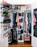 Open closet with colorful clothes, shoe rack on door, and boxes on top shelf next to a white dresser with a mirror.
