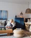 Cozy living room with a wood-burning stove, blue cabinet, and a woman lighting candles on a wooden coffee table.