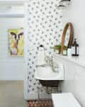 Bathroom with bee-patterned wallpaper, white sink, round mirror, and cow painting on the wall.