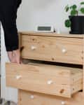 A woman putting items away in a natural wood dresser.