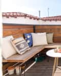 Rooftop patio with wooden bench, colorful cushions, round white table, and potted cacti on a shelf.