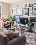 Living room with gray sofa, gallery wall, TV, plants, and a small dining table by the window.