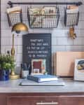 a home office space is carved out of a small corner of a kitchen and features small gold lamp and hanging baskets for organization