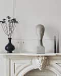 Marble fireplace mantel with a head sculpture, black vase, white lamp, and decorative cones.
