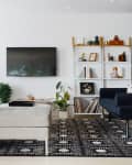 Modern living room with a navy sofa, wall-mounted TV, patterned rug, and white shelving with books and decor.
