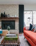 Living room with orange sofa, blue armchair, stone fireplace, and decorative vases on mantel.