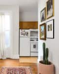 Hallway with a round mirror, table lamp, potted cactus, framed art, and view into a kitchen with white appliances.