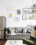 Living room with gray sofa, dog, wall art, bookshelves, green armchair, and stainless steel fridge.