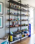 Children's room with shelves of LEGO sets, framed state art, and a loft bed near large windows.