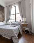 Bedroom with exposed brick wall, metal bed frame, striped bedding, books, and a wicker nightstand with a lamp.