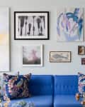 Blue sofa with floral pillows, surrounded by eclectic wall art, including abstract and black-and-white pieces.