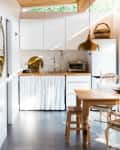 Small kitchen with white cabinets, wooden countertop, toaster oven, and a dining table with chairs under a sloped wooden ceiling.