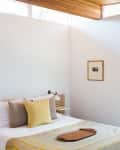 A white-walled bedroom with patterned bedding and a yellow throw pillow