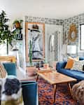 Living room with blue sectional sofa, patterned pillows, wooden coffee table, large wall art, and geometric wallpaper.