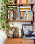 Kitchen with white cabinets and a black countertop, adjacent to a bookshelf filled with colorful books and a hanging plant.