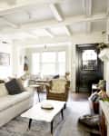 Living room with white sofa, gray pillows, wooden chairs, coffee table, and fireplace, featuring a guitar on the wall.