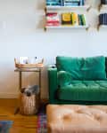 Green velvet sofa with a tan ottoman, bookshelves, and a small table beside a staircase.