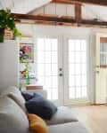 Cozy living room with white French doors, striped pillows on a daybed, and plants on shelves.