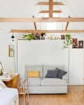 Cozy living room with a gray sofa, wooden beams, hanging plants, and a small side table on a wooden floor.