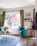 Living room with a blue velvet sofa, palm plant, glass coffee table, and framed photos on the wall.