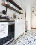 Galley kitchen with patterned tile floor, open shelves, stainless steel stove, and fridge with magnets.