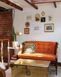 Cozy living room with orange sofa, wicker chairs, gold coffee table, brick wall, and framed art.