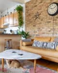 Living room with tan leather sofa, marble coffee table, brick wall, and a cat on a patterned rug.