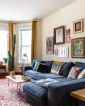 Living room with a blue sectional sofa, colorful pillows, gallery wall art, mustard curtains, and a cactus by the window.