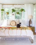 Bohemian bedroom with a cat on a colorful bedspread, hanging plants, and decorative lamps on side tables.
